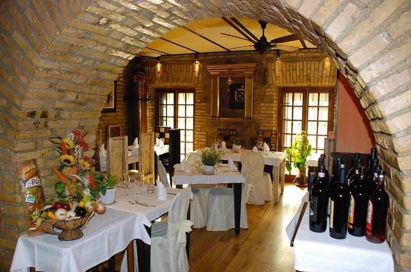 Sala con volta in mattoni a vista, tavoli apparecchiati di bianco e bottiglie di vino in primo piano.