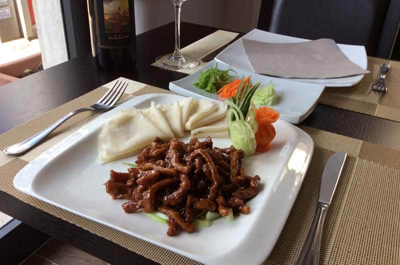 Piatto con strisce di carne in salsa scura, involtini sottili e decorazioni di carota e cetriolo intagliati.