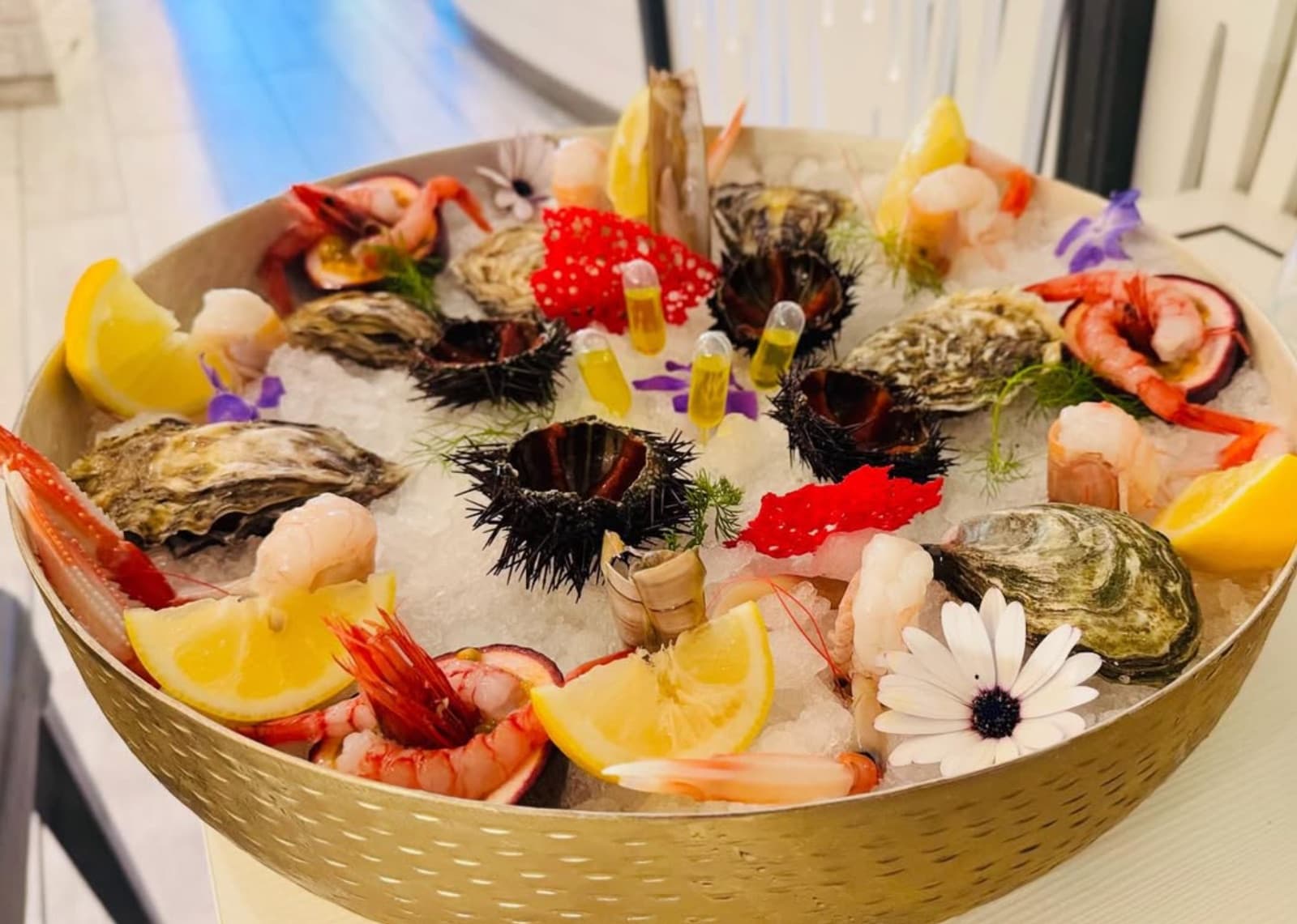 Grande vassoio dorato su ghiaccio con ostriche, ricci di mare, gamberi, fette di limone e fiori commestibili.