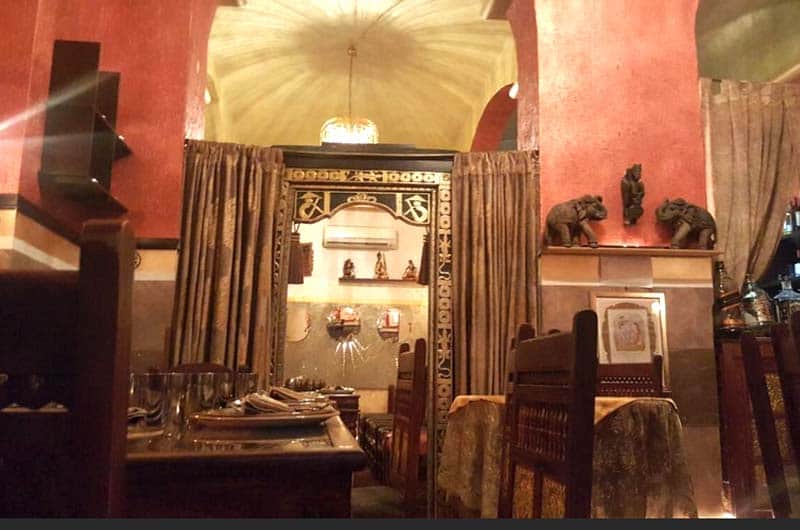 Sala con archi in muratura, tende dorate e statuette di elefanti su una mensola alla parete.