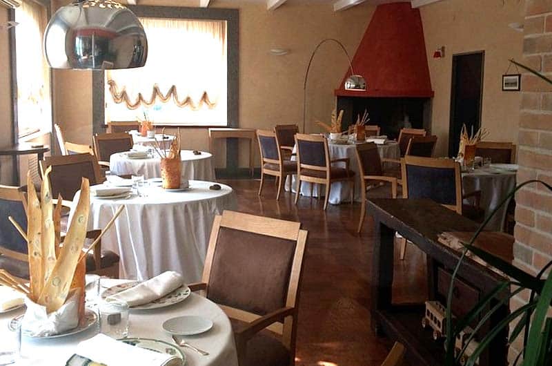 Sala da pranzo con tavoli rotondi apparecchiati in bianco, sedie imbottite blu e un camino conico rosso sul fondo.