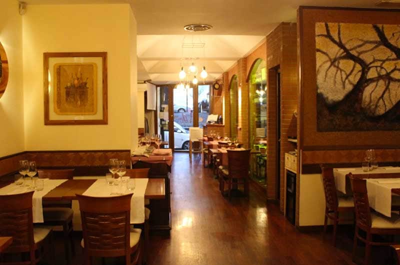 Sala da pranzo con tavoli apparecchiati, pareti in mattoni, dipinto di un albero e finestre ad arco sulla destra.