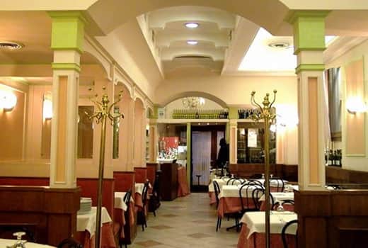 Sala di ristorante con colonne verdi, tavoli con tovaglie bianche e rosa e soffitto ad arco illuminato.