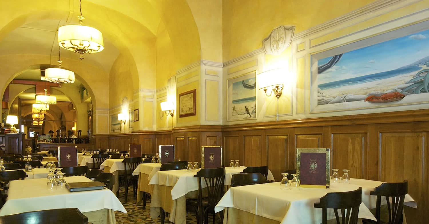 Sala da pranzo con soffitto a volte gialle, pannellature in legno e tavoli apparecchiati con tovaglie bianche.