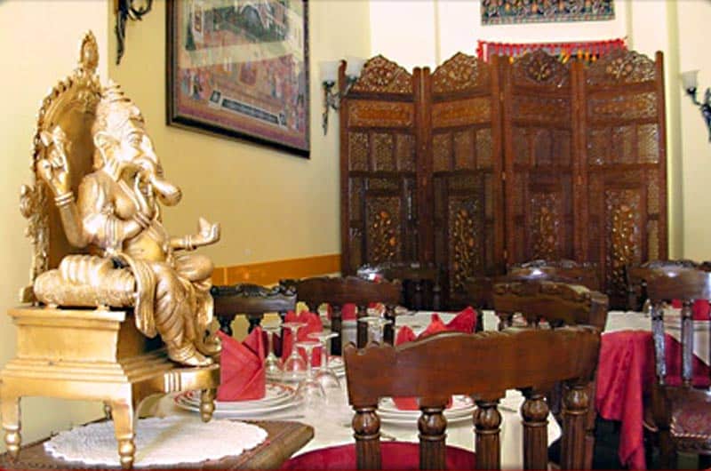 Statua dorata di Ganesh su un trono ligneo accanto a tavoli apparecchiati con tovaglioli rossi.