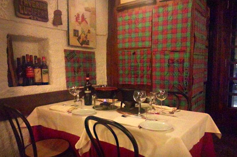 Tavolo apparecchiato con calici da vino davanti a pareti rivestite di tessuto scozzese rosso e verde.