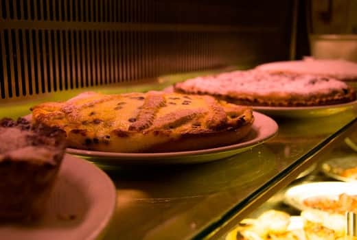 Crostate su piatti bianchi in una vetrina illuminata, con altri vassoi di cibo sullo sfondo.