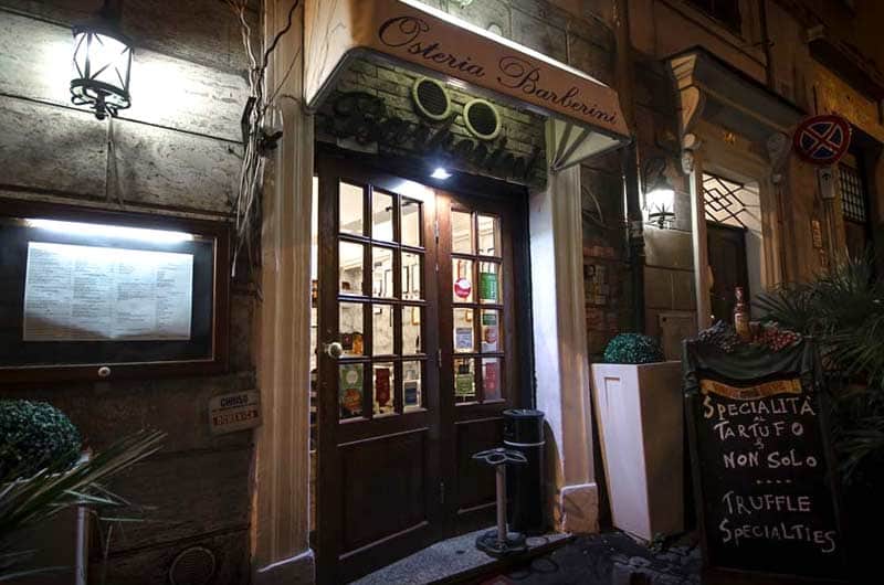 Ingresso serale con insegna luminosa, porta a vetri in legno e lavagna con scritta Truffle Specialties.