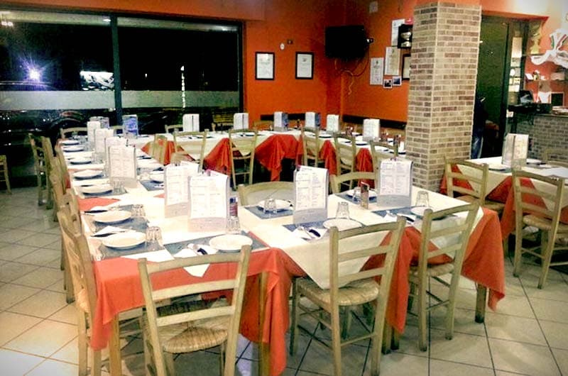 Sala di ristorante con tavoli apparecchiati e tovaglie bianche coperte da teli rossi.