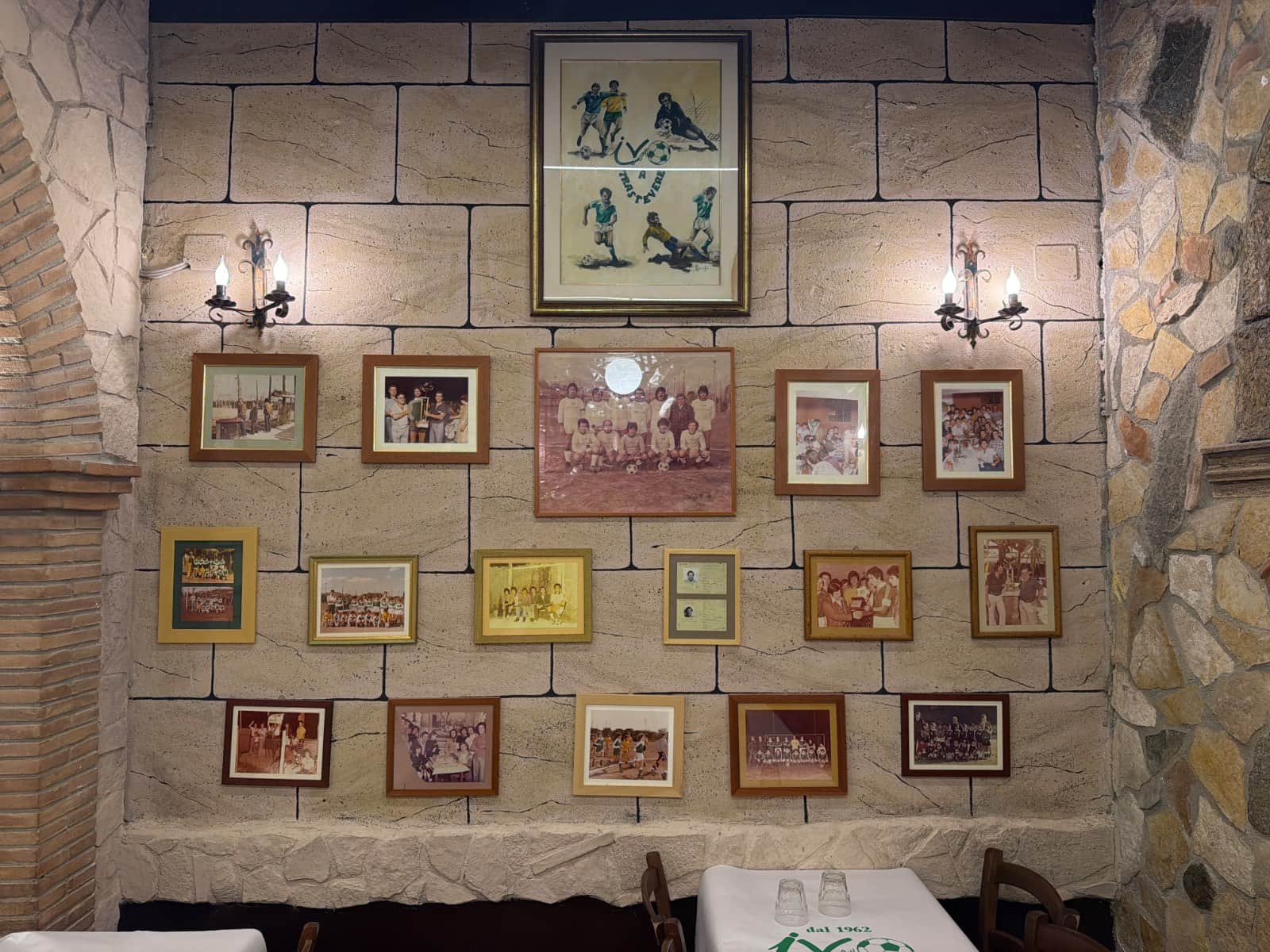 Parete in pietra con una grande illustrazione di calciatori in alto e sotto molte foto d'epoca di squadre di calcio in cornici diverse.