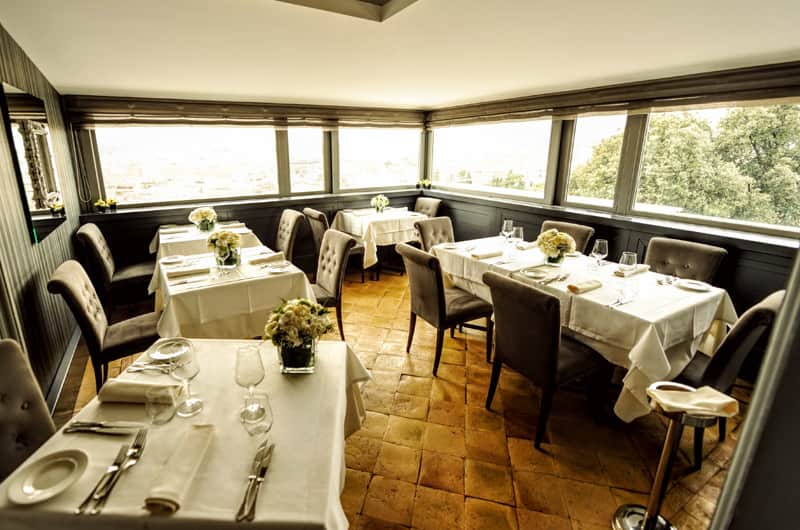 Sala da ristorante con vetrate panoramiche, tavoli apparecchiati con tovaglie bianche e composizioni di fiori.