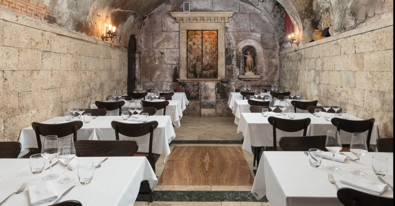 Sala da pranzo con volta in pietra antica, tavoli bianchi e sedie scure disposti lungo le pareti.