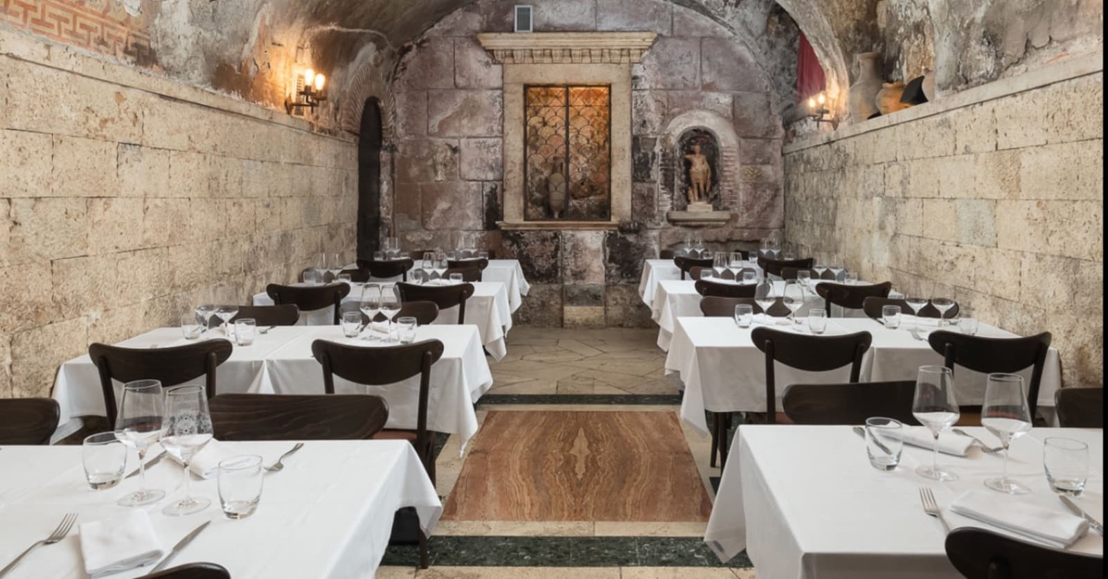 Sala da pranzo con volta in pietra antica, tavoli bianchi e sedie scure disposti lungo le pareti.