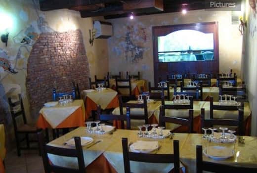 Sala con tavoli apparecchiati di giallo e arancio, parete in mattoni a vista e schermo sul fondo.