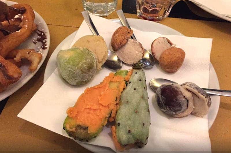 Piccole sfere di gelato colorate con cucchiaini infilati, accanto a due frutti tagliati a metà con buccia verde a puntini.
