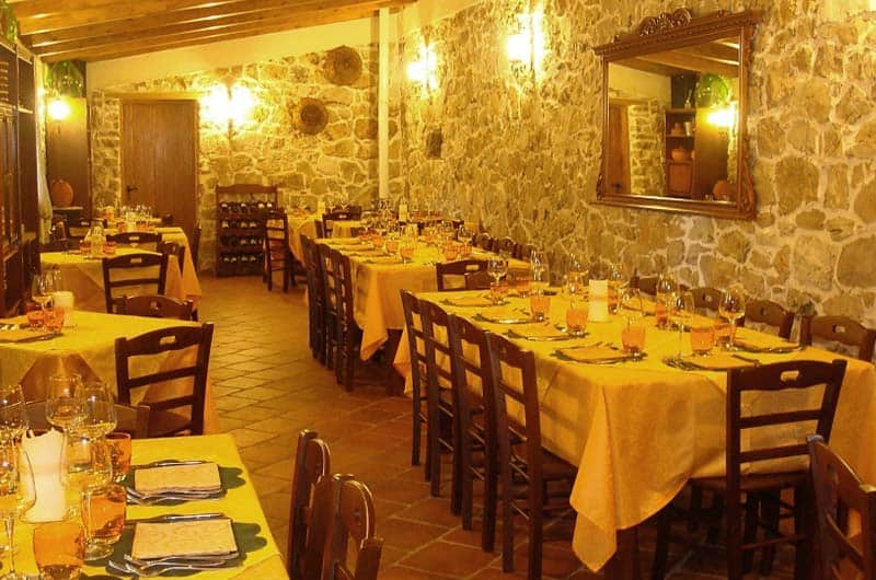 Sala da pranzo in pietra a vista con tavoli apparecchiati di tovaglie gialle e sedie in legno scuro.
