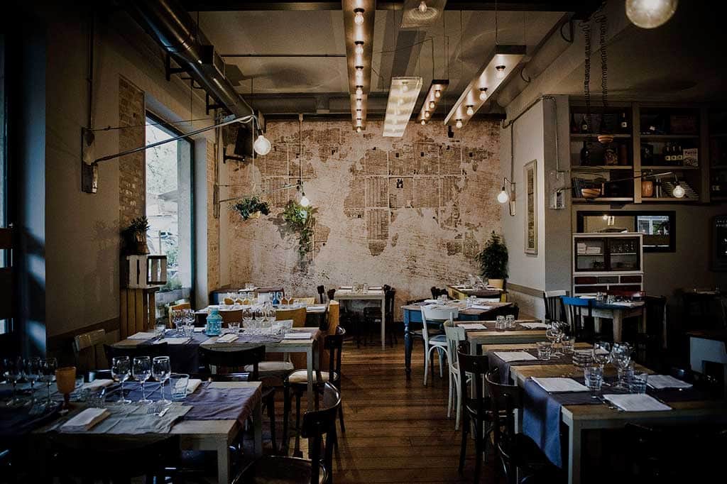 Sala con tavoli apparecchiati in legno, muro in mattoni con una grande mappa del mondo dipinta sullo sfondo.