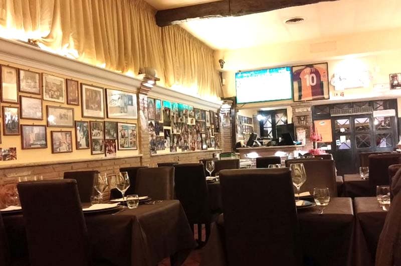 Sala di ristorante con tavoli apparecchiati e sedie scure, pareti coperte di foto incorniciate.