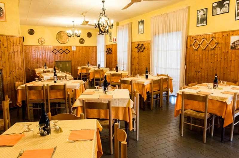 Sala di ristorante con tavoli apparecchiati in bianco e arancione, pareti in legno e lampadari in ferro battuto.