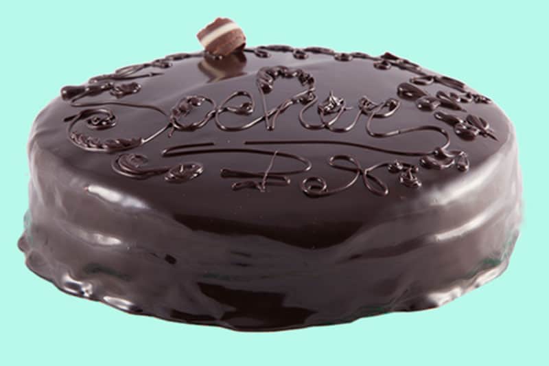 Torta rotonda con glassa di cioccolato lucida e decorazioni a filo di cioccolato in stile corsivo.