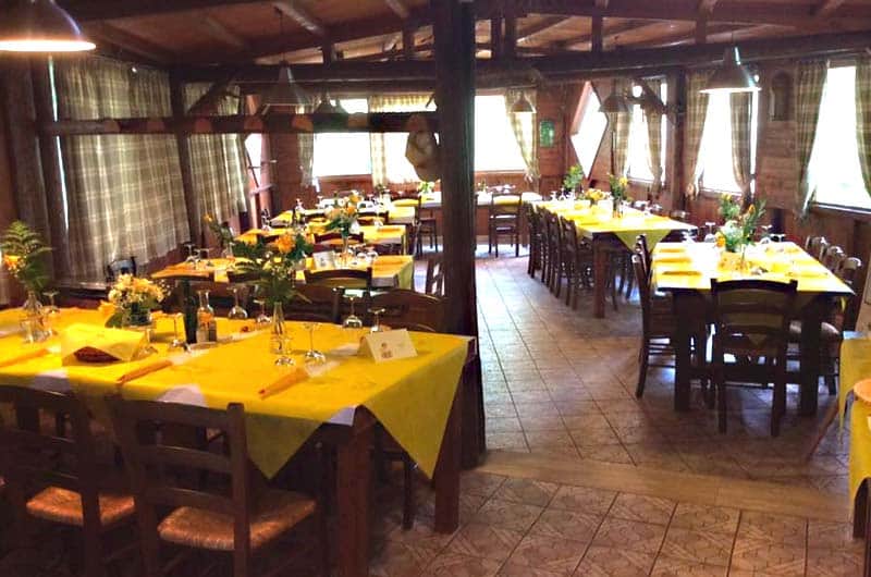 Sala da ristorante in legno con tavoli apparecchiati con tovaglie gialle e sedie in legno impagliate.