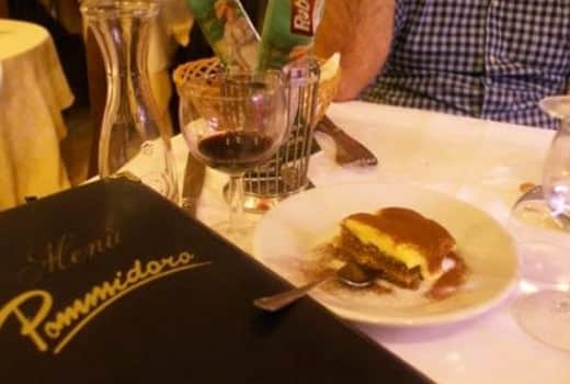 Copertina nera con scritta dorata «Menù Pommidoro» e una forchetta sopra, dietro un piatto con un dolce a strati e un bicchiere di vino.