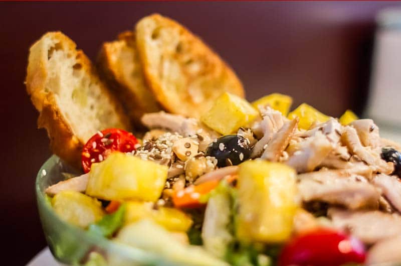 Insalata con pollo sfilacciato, cubetti di ananas, pomodorini e olive nere, servita con fette di pane tostato.