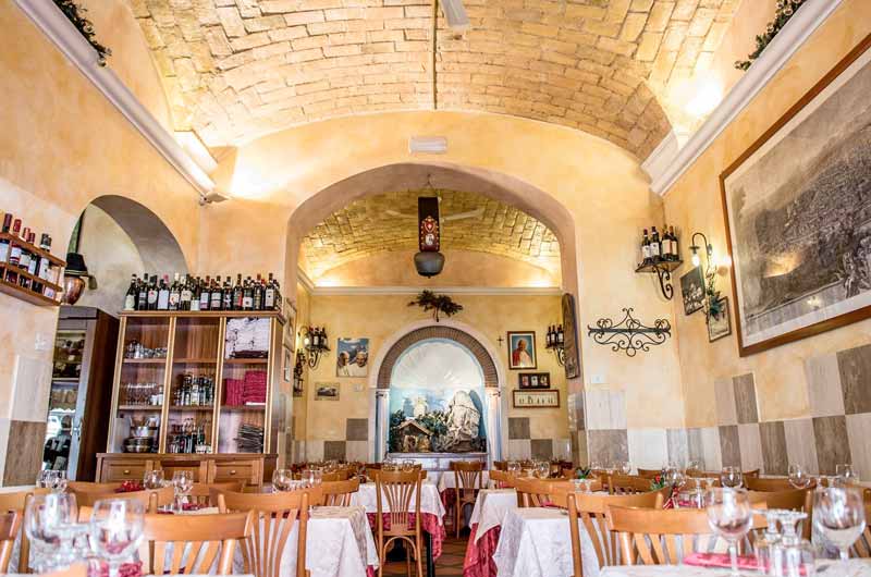 Sala da pranzo con soffitto a volta in mattoni, tavoli apparecchiati con tovaglie bianche e rosse.