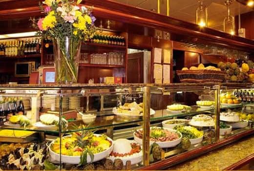 Banco gastronomia con vetrina refrigerata piena di insalate e piatti pronti in ciotole bianche.