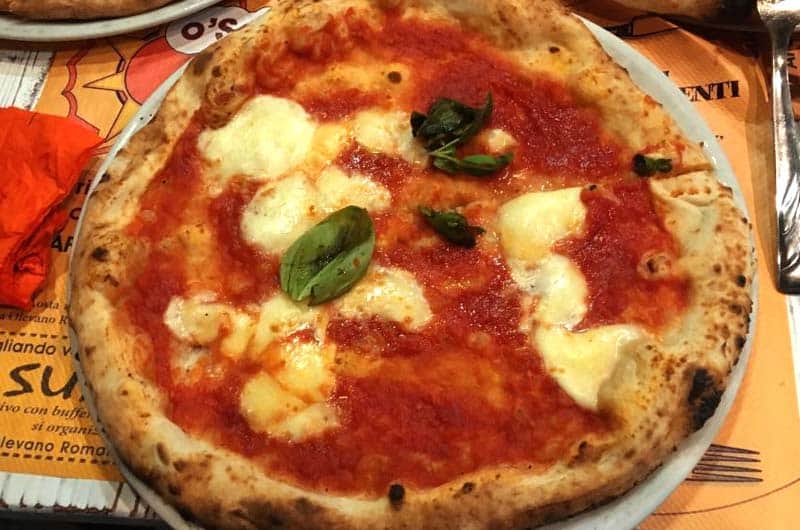 Pizza margherita con mozzarella filante, pomodoro e foglie di basilico fresco su piatto bianco.