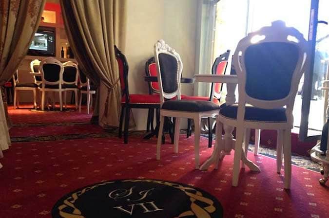 Sala con sedie imbottite bianche e nere, tende beige, tappeto rosso e stemma circolare a terra.