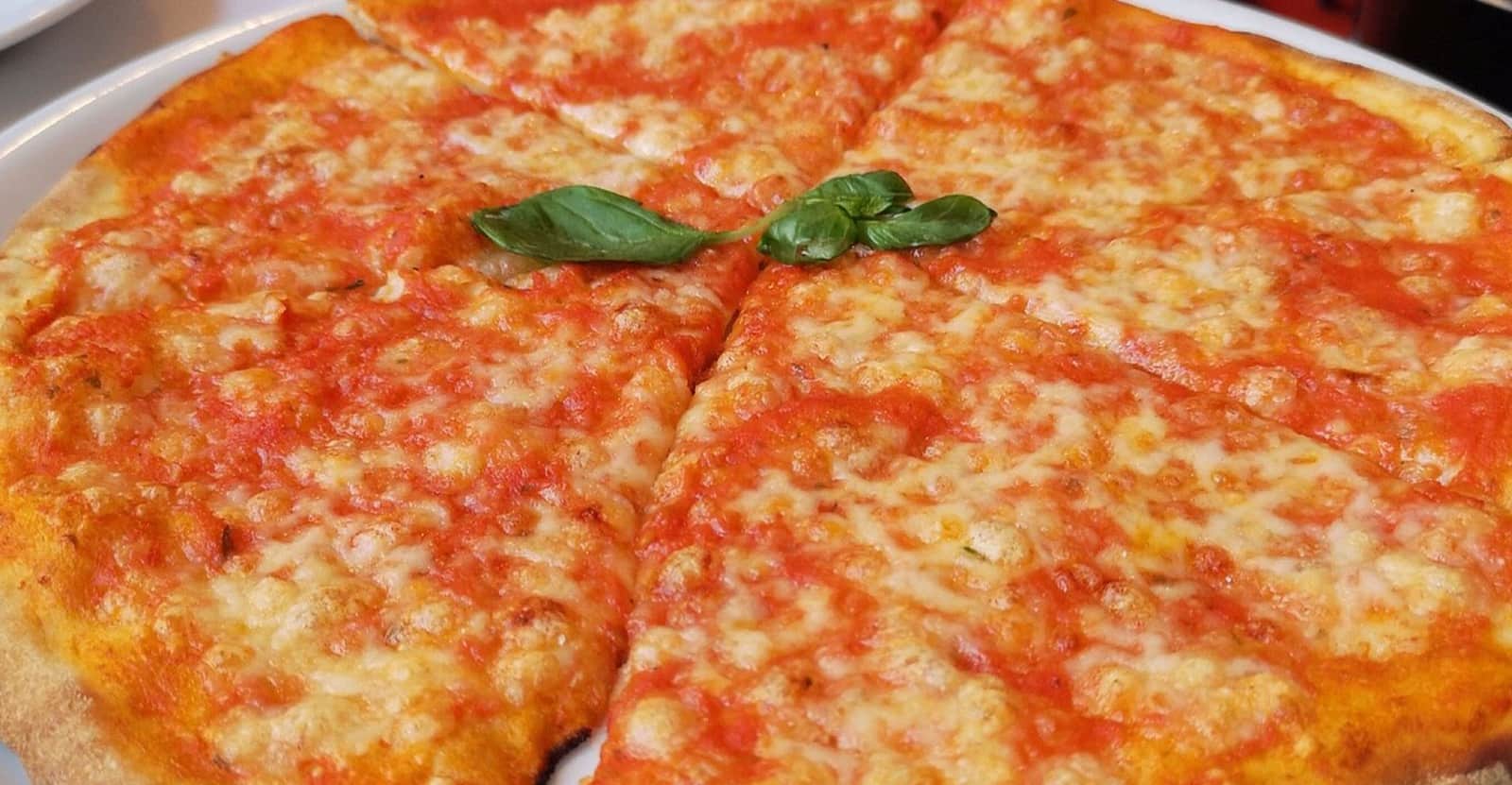 Pizza tonda tagliata a spicchi con pomodoro e mozzarella fusa, due foglie di basilico al centro.
