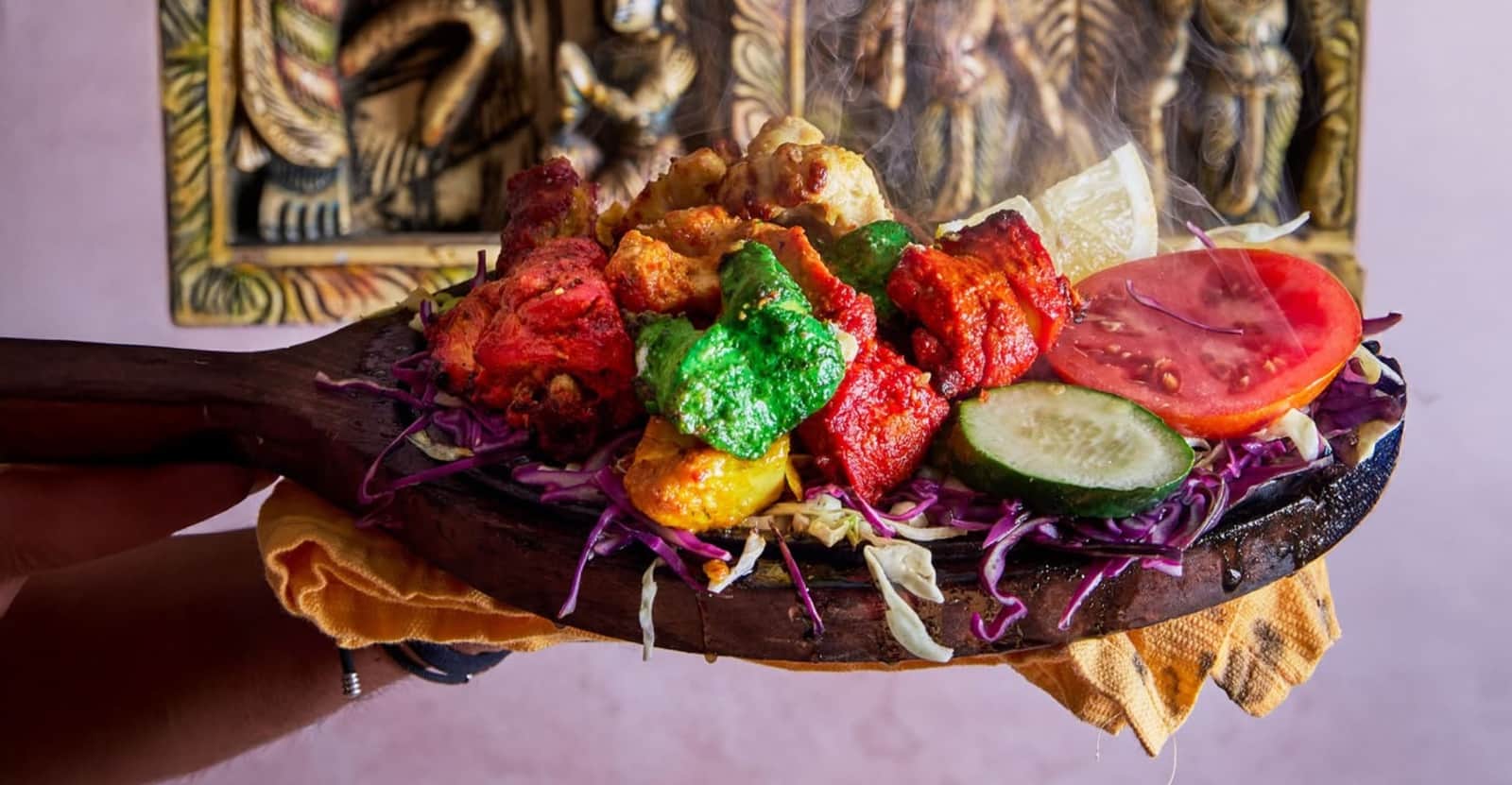 Piatto in legno con spiedini tandoori rossi, verdi e arancioni su letto di cavolo viola, fumante.