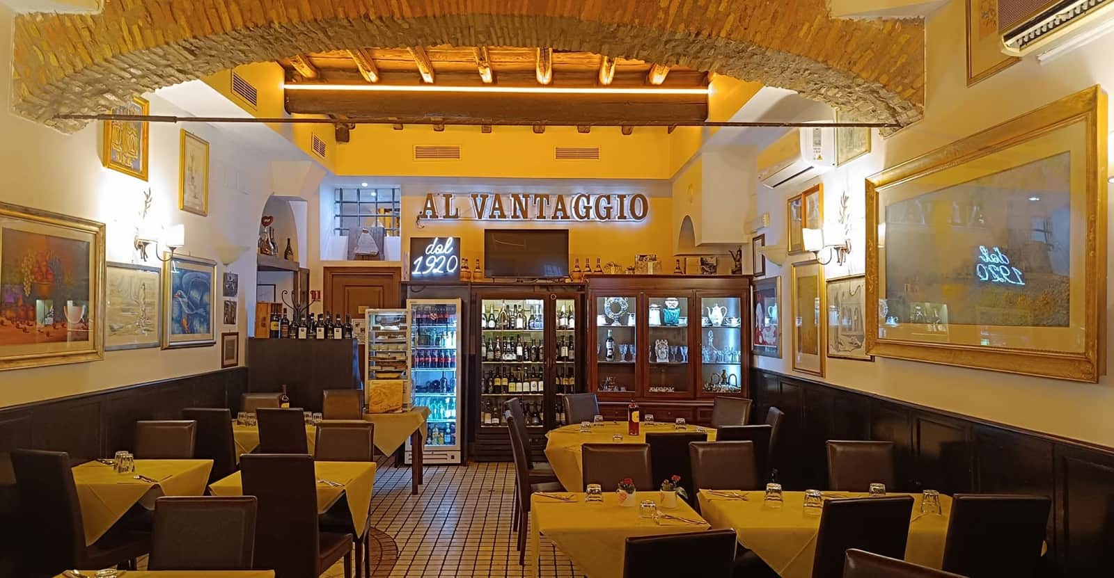 Sala con soffitto a volta in mattoni, tavoli con tovaglie gialle e scritta AL VANTAGGIO sulla parete di fondo.