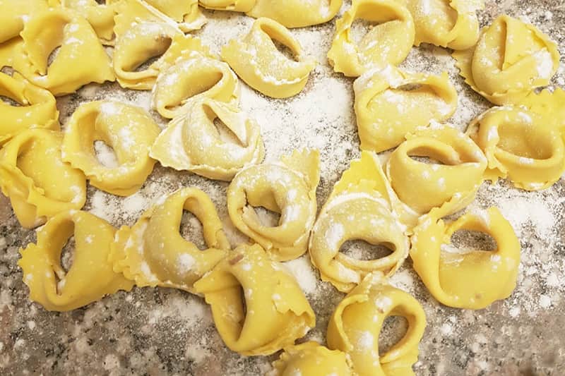 Tortellini di pasta fresca gialla disposti su un piano infarinato, visti dall'alto.