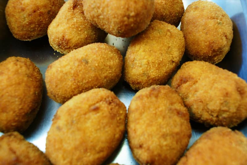 Crocchette ovali impanate e fritte, disposte una accanto all'altra in un vassoio metallico.