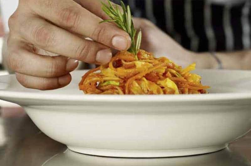 Una mano guarnisce con un rametto di rosmarino un piatto di tagliolini al sugo di pomodoro.