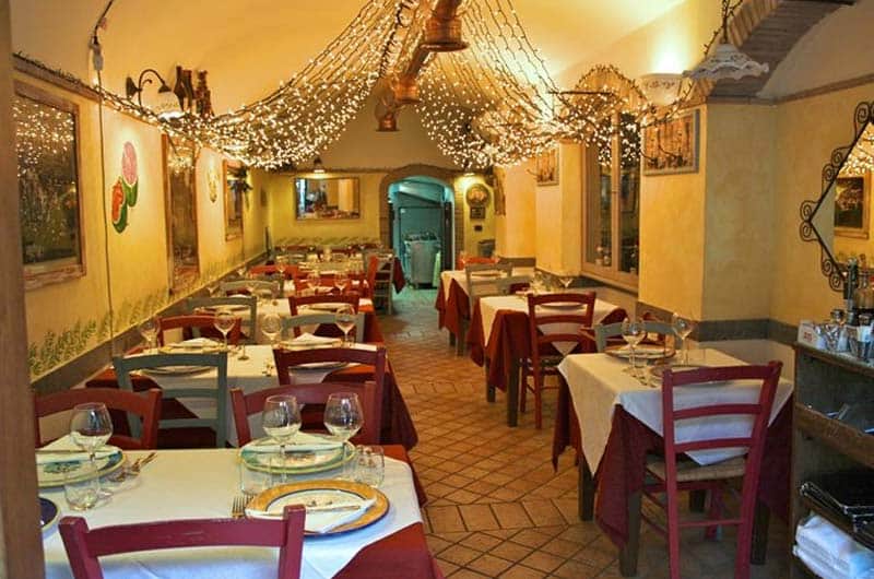 Sala da ristorante con tavoli apparecchiati di rosso, soffitto a volta con luci decorative sospese.