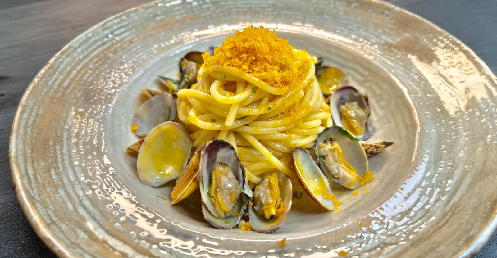 Spaghetti con vongole e cozze aperte, sormontati da un ciuffo di polvere dorata, su piatto in ceramica chiara.