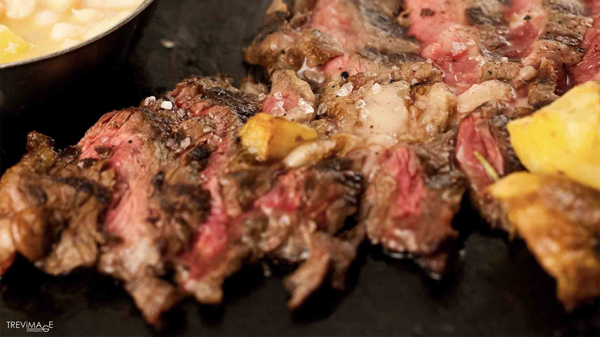 Carne alla griglia tagliata a fette, rosa all'interno e scura in superficie, con grani di sale grosso e patate a spicchi.