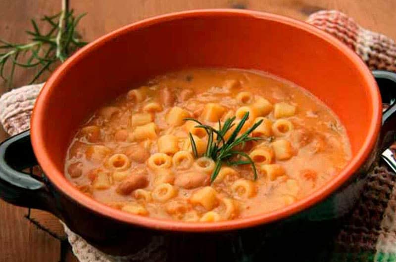 Zuppa di pasta corta, fagioli e patate in una ciotola di terracotta arancione con manici neri.