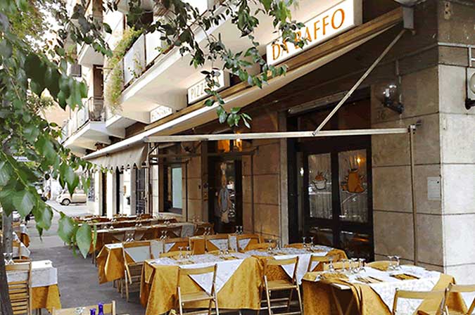 Dehors con tavoli rotondi e tovaglie dorate sotto una tenda da sole, insegna DA BAFFO sulla facciata.