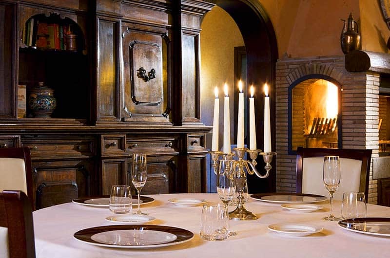 Candelabro d'argento con cinque candele accese al centro di un tavolo apparecchiato con piatti e calici.