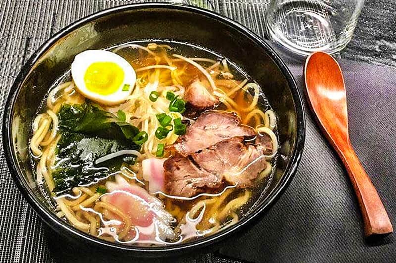 Ciotola di ramen con uovo sodo, fette di carne, cipollotto e verdure a foglia in brodo.
