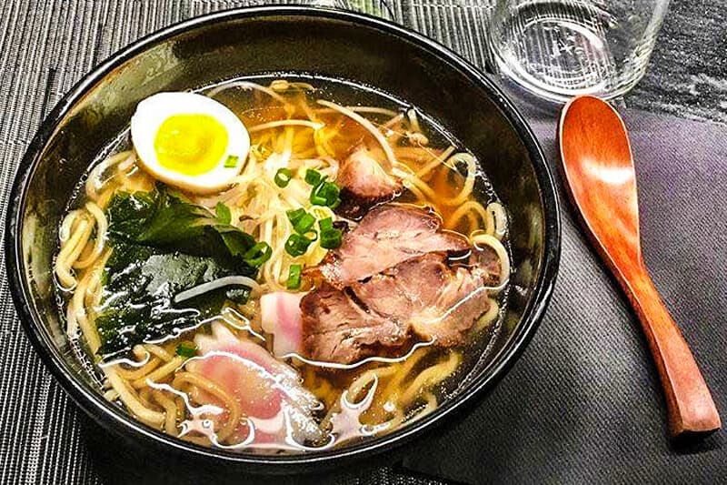 Ciotola di ramen con uovo sodo, fette di carne, cipollotto e verdure a foglia in brodo.