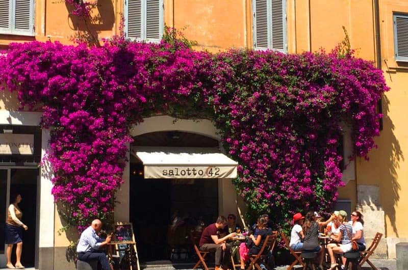 Facciata color ocra coperta di bouganville fucsia, con tavolini all'aperto sotto l'insegna salotto 42.