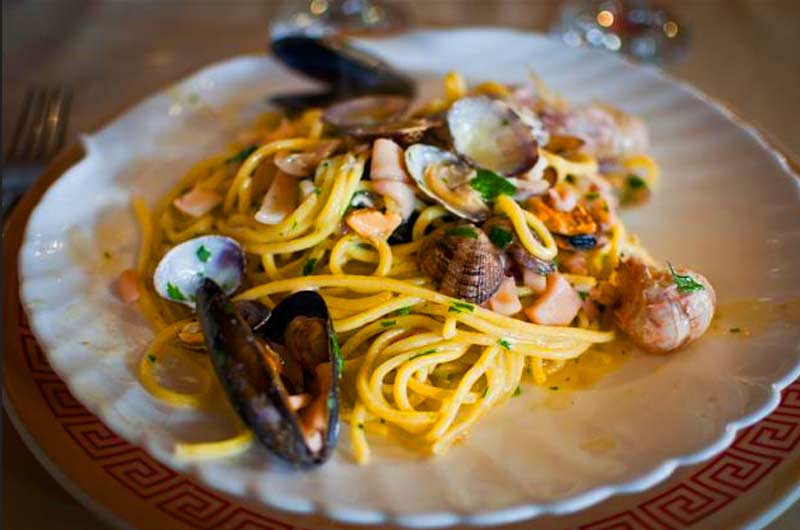 Spaghetti con cozze, vongole e gamberi su piatto bianco con bordo rosso decorato.