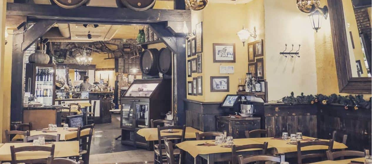 Sala di un ristorante con travi in legno scuro, botti sospese e tavoli con tovaglie gialle.