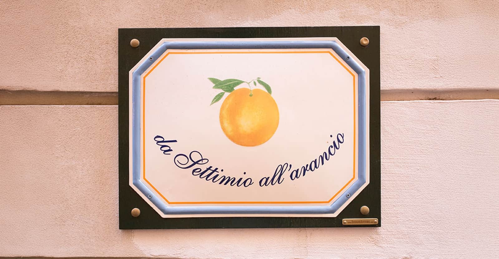 Targa decorativa con un'arancia dipinta e la scritta "da Settimio all'arancio" su parete rosa.
