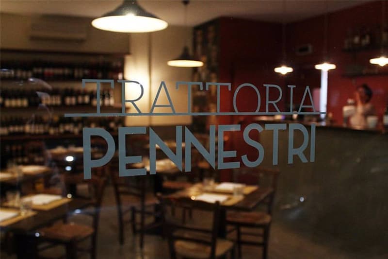 Scritta 'Trattoria Pennestri' su una vetrina, con tavoli apparecchiati e scaffali di vino visibili all'interno.